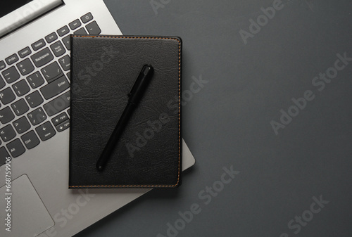Laptop and Notebook with black leather cover, pen on dark gray background