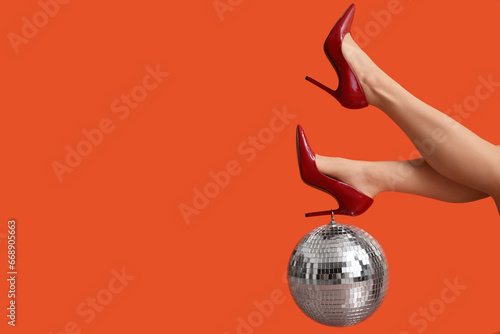 Female legs in stylish high heels with disco ball on red background