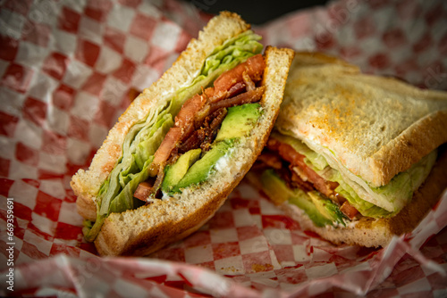 Bacon Lettuce Tomato Avocado sandwhich served diner style on red and white checkered paper