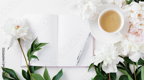 Top view of morning coffee cup, diary and white peonies flowers on white table