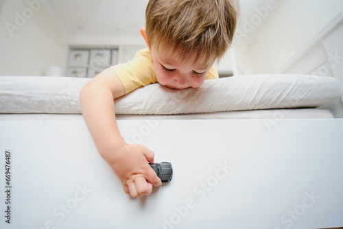 The child is playing alone on the bed and might fall down if not taken care of. Kid aged two years (two-year-old boy)