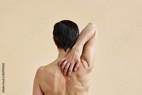 Minimal rear view of adult woman scratching bare back against beige background, copy space