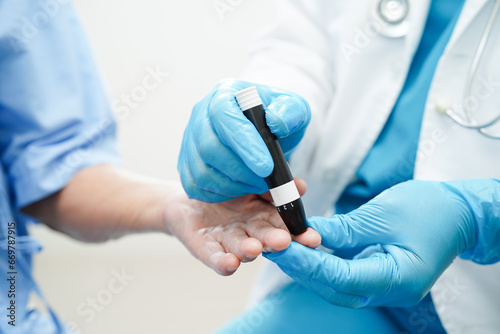 Asian doctor using lancet pen on senior patient finger for check sample blood sugar level to treatment diabetes.