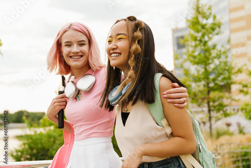 Two cheerful girls hugging while walking together in park