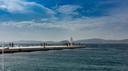 Small white lighthouse and people on pier. Seascape view from Zadar, Croatia.