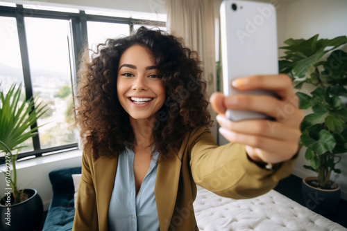 A young latin woman is is making a selfie while smiling with a telephone in a modern living room a high tech social media woman