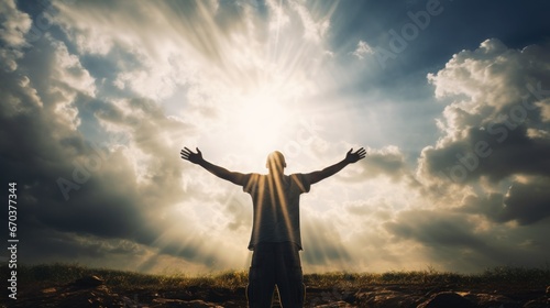 A man standing alone and spreading his hands with joy and inspiration while facing the sun and the sky. Happiness, liberty, freedom, and independence concept