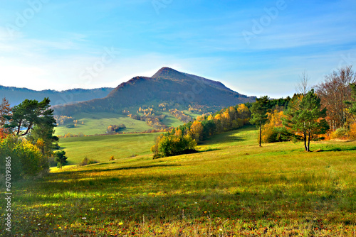 Autumn mountains landscape. Trees on a slope with dry grass and wooded mountains under blue sky with white clouds. View of Mountain Lackowa (997 msl) in Low Beskids. (Beskid Niski)