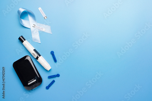 Diabetes awareness concept of ribbon glucose meter test strips and lancets on blue background flat lay. Diabetes awareness concept