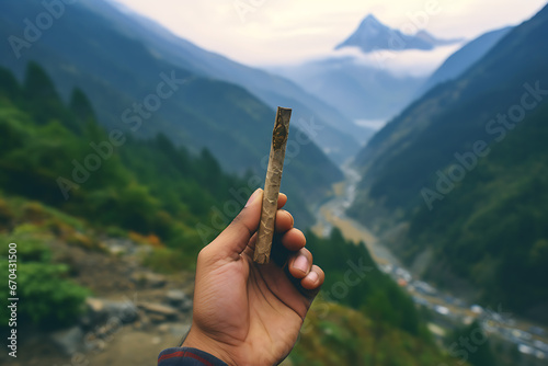 Hand holding a smoking joint in the himalaya, weed, mountains, himalaya mountains in the bacckground