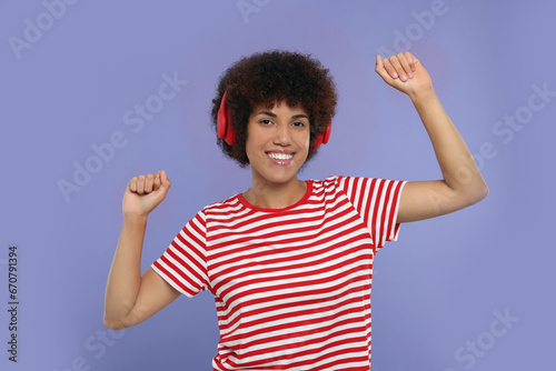 Happy young woman in headphones enjoying music on purple background