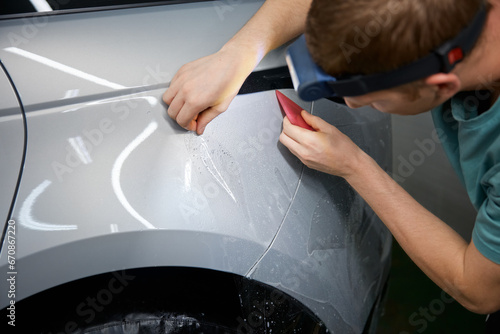 Closeup master hand with rubber scraper applying sticking protective film on car