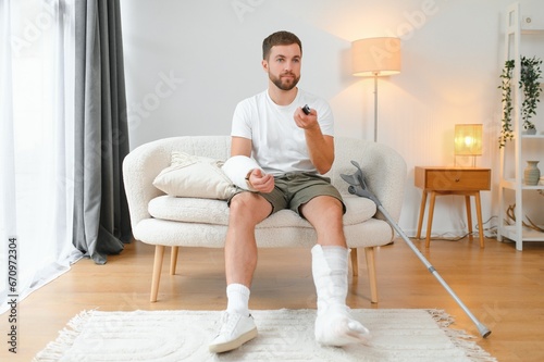 man recovery from accident fracture broken bone injury with leg splints in cast neck splints collar arm splints sling support arm in living room. Social security and health insurance concept