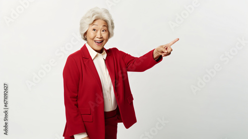 Surprised senior asian lady pointing upper left corner, checking out promo offer and smiling amazed, standing in red blazer over white background