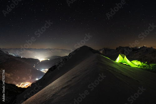 Winterbiwak im Schnee auf einem Berg in den Alpen mit grünem Zelt bei sternenklarem Nachthimmel