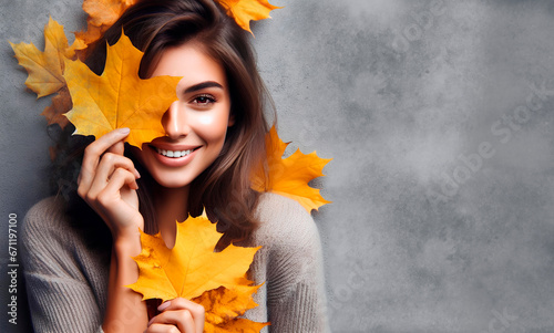 mujer sonriendo con hojas de color anaranjado en las manos, pullover de lana gris y fondo gris, concepto de otoño 