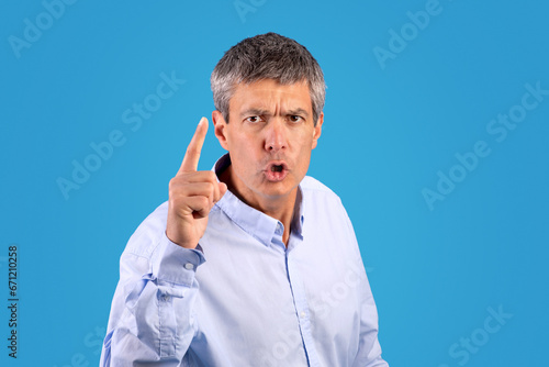 strict mature man shaking finger looking at camera, blue background