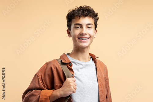 Portrait handsome teenage boy with dental braces wearing casual clothes isolated on beige background