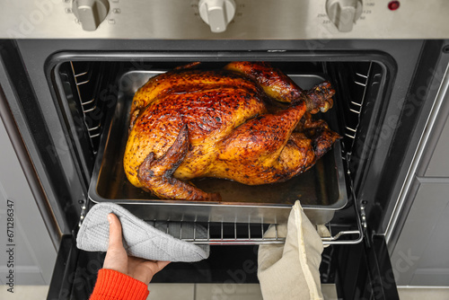 Woman taking tasty baked turkey from oven in kitchen. Thanksgiving Day celebration