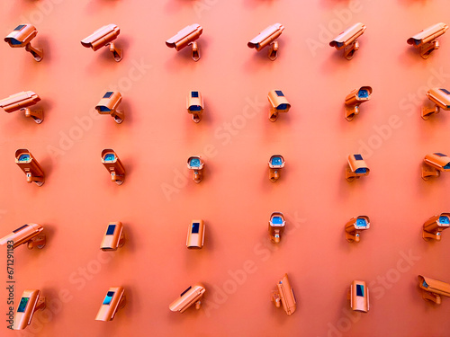 Horizontal photography of a bunch of CCTV cameras pointing in all directions mounted on an orange wall. 