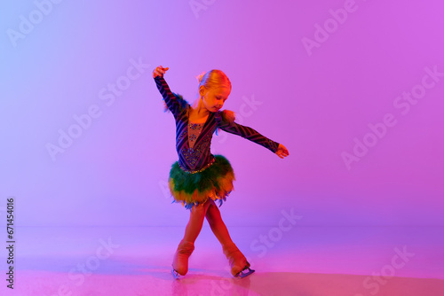 Beautiful, adorable little girl, child in stage costume dancing, performing figure skating against gradient pink purple background in neon. Concept of childhood, figure skating sport, hobby, school