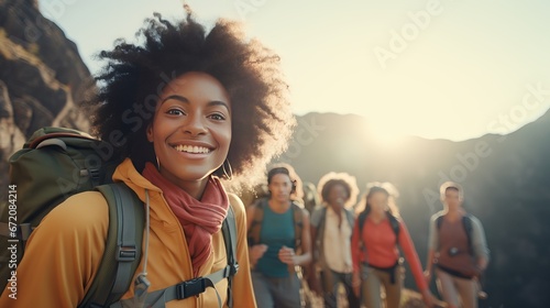 Upbeat youthful african lady eating sandwich and grinning whereas unwinding with companions amid climb. Gather of climbers taking break amid nation climb