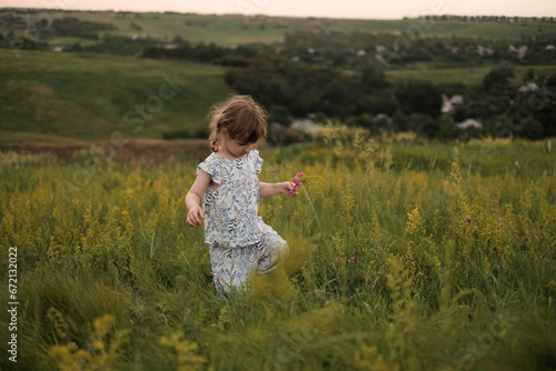 Little girl collecting wild flowers at the meadow at warm summer evening