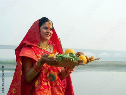 A woman offering prasad fruits vegetables and other items and a Diya to pray sun God at a lake during Chhath Puja. Hindu devotees worship God sun with a ritual while standing in a river - Hindu ...