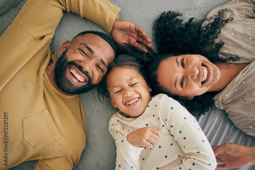 Happy family, above and kid smile or happy with parents together in the morning laughing in a bedroom on a bed. Relax, mom and dad enjoy quality time with kid with happiness, bonding and love