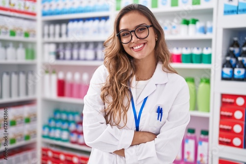 Young beautiful hispanic woman pharmacist smiling confident standing with arms crossed gesture at pharmacy