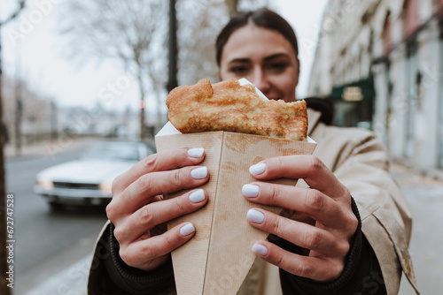 hispanic woman eating delicious crepes in the streets of Paris city, hands holding pancakes 
