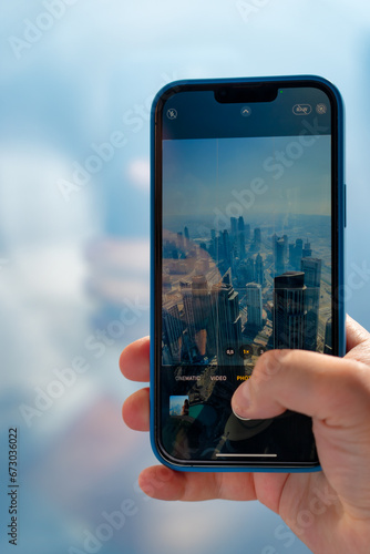 A young man takes a picture of a tall building in Dubai with his mobile phone.