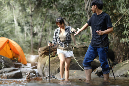 Asian Teenagers walk in the natural stream with a camping tent in the background, Enjoying the relaxing atmosphere of the surrounding nature.