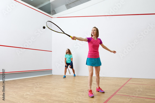 Happy millennial-age couple characters playing game of racquetball together