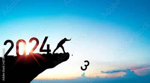 Silhouette man pushing number 3 from cliff with 2024 on blue sky for preparation merry Christmas and happy new year from 2023 to 2024 concept.