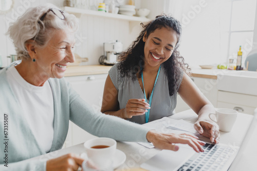 Side view of young black female volunteer social worker teaching senior caucasian lady how to use laptop, wireless internet, browsing web pages, reading news, showing her new skills