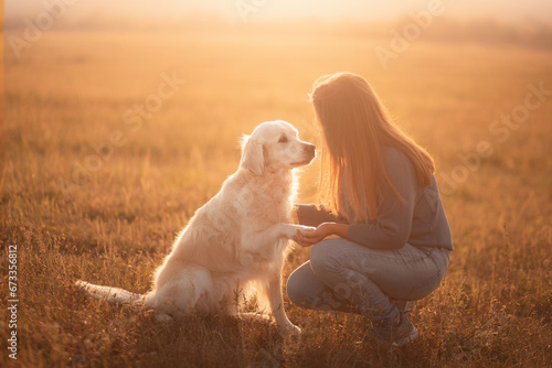 golden retriever dog and a young woman sharing a moment at sunset doing the paw trick