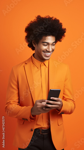 Enthusiastic Young Entrepreneur Excitedly Showcases Mobile Application Potential on a Blank Smartphone Screen Amidst a Vivid Orange Studio Backdrop
