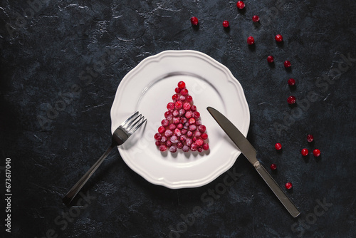 Table setting with Christmas decor. Symbol Christmas tree from a frozen red berries on the white plate and black background