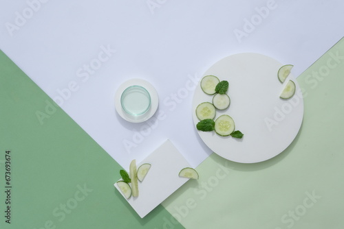 On the green and white background, white geometric podiums with fresh cucumber slices decorated. Advertising photo for product with natural extract. Top view, flat lay
