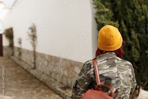 Mujer con mochila y cazadora militar con gorra de lana de color mostaza paseando por una calle