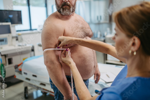 Female doctor measuring arm circumference of overweight patient using tape measure. Obesity affecting middle-aged men's health. Concept of health risks of overwight and obesity.