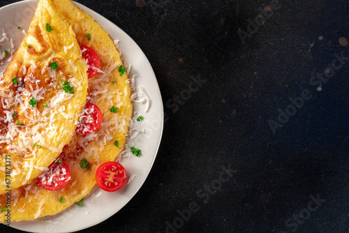 An omelet with tomato and parsley, eggs for breakfast, a healthy vegetarian dish with cheese, overhead flat lay shot with copy space