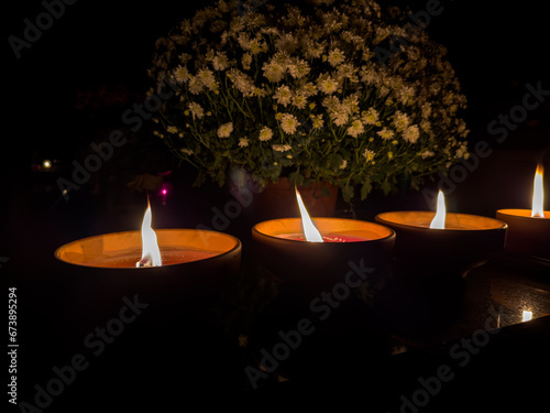 trzy ceramiczne znicze płonące na nagrobku stojące obok kwiecistej chryzantemy