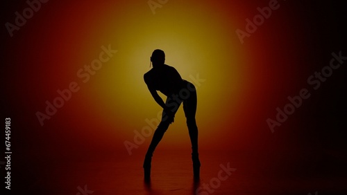 Woman dancer silhouette in high heels standing in the studio in yellow spotlight. Isolated on colorful background.