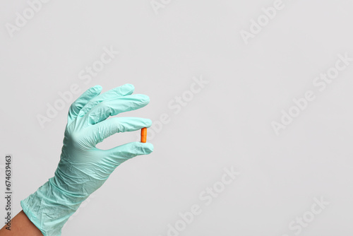 Hand of doctor in turquoise glove with pill on grey background