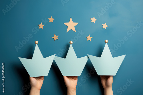 Flat lay with three simple paper kings crowns on kids hands and gold stars on blue background, children craft. Three Kings day, Epiphany day concept