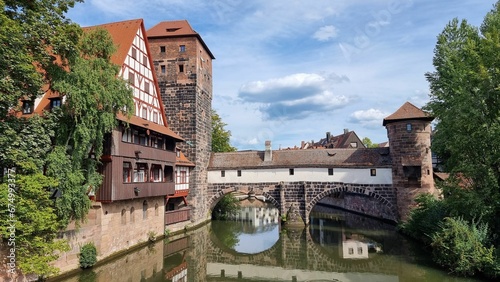 Situated near a body of water, in a setting of various buildings, a bridge, and trees in Nuremberg