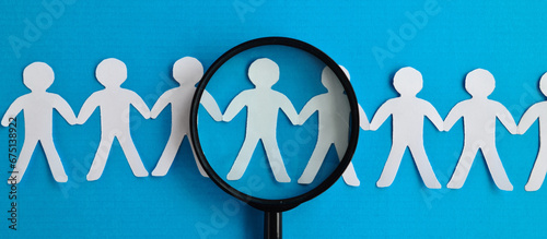 Abstract paper figures of people under black magnifying glass on a blue background