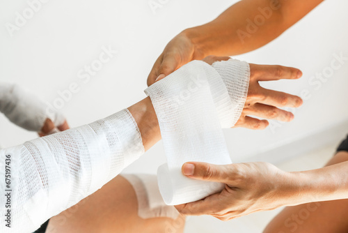 Sister wrapping her brother wrist and arm with bandage around injured hand over white background at home. First aid, accident and injury treatment concept. Closeup